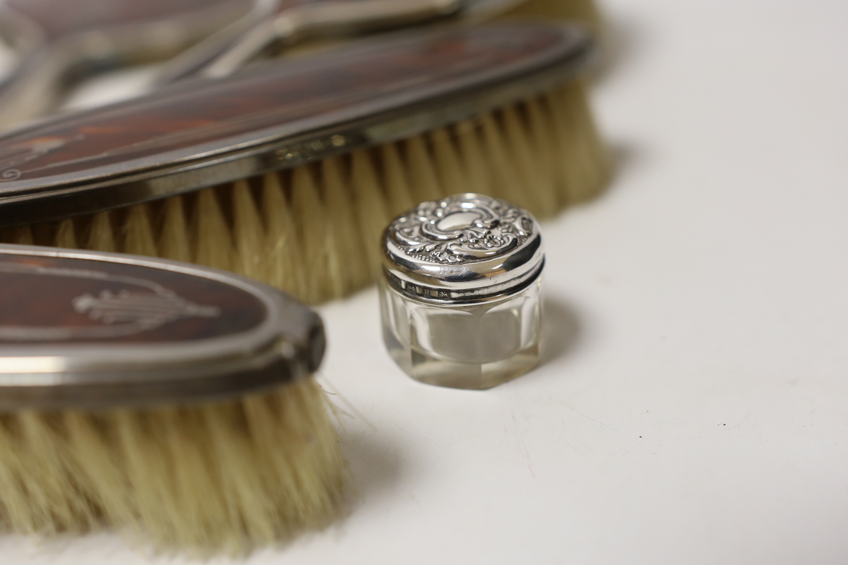 A George V silver and tortoiseshell pique mounted dressing table set, Adie Bros, Birmingham, 1934, and three silver topped toilet jars.